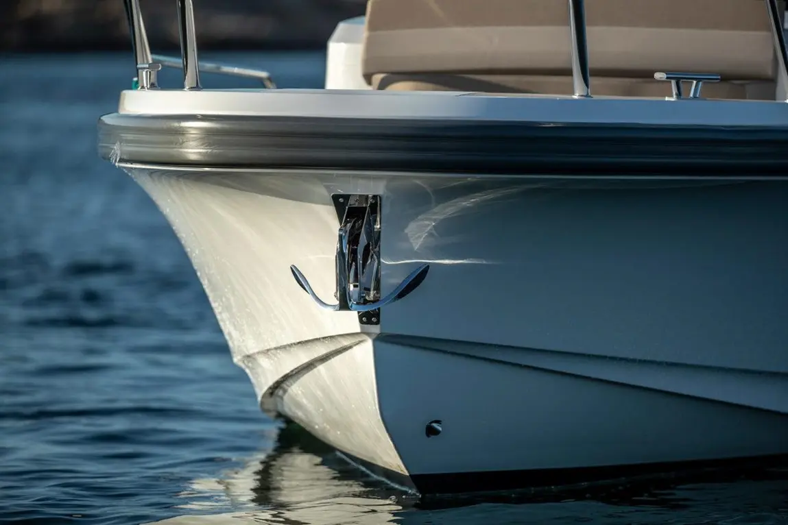 A close-up of a boat's bow with a polished anchor and reflections on water, showcasing maritime craftsmanship and design.